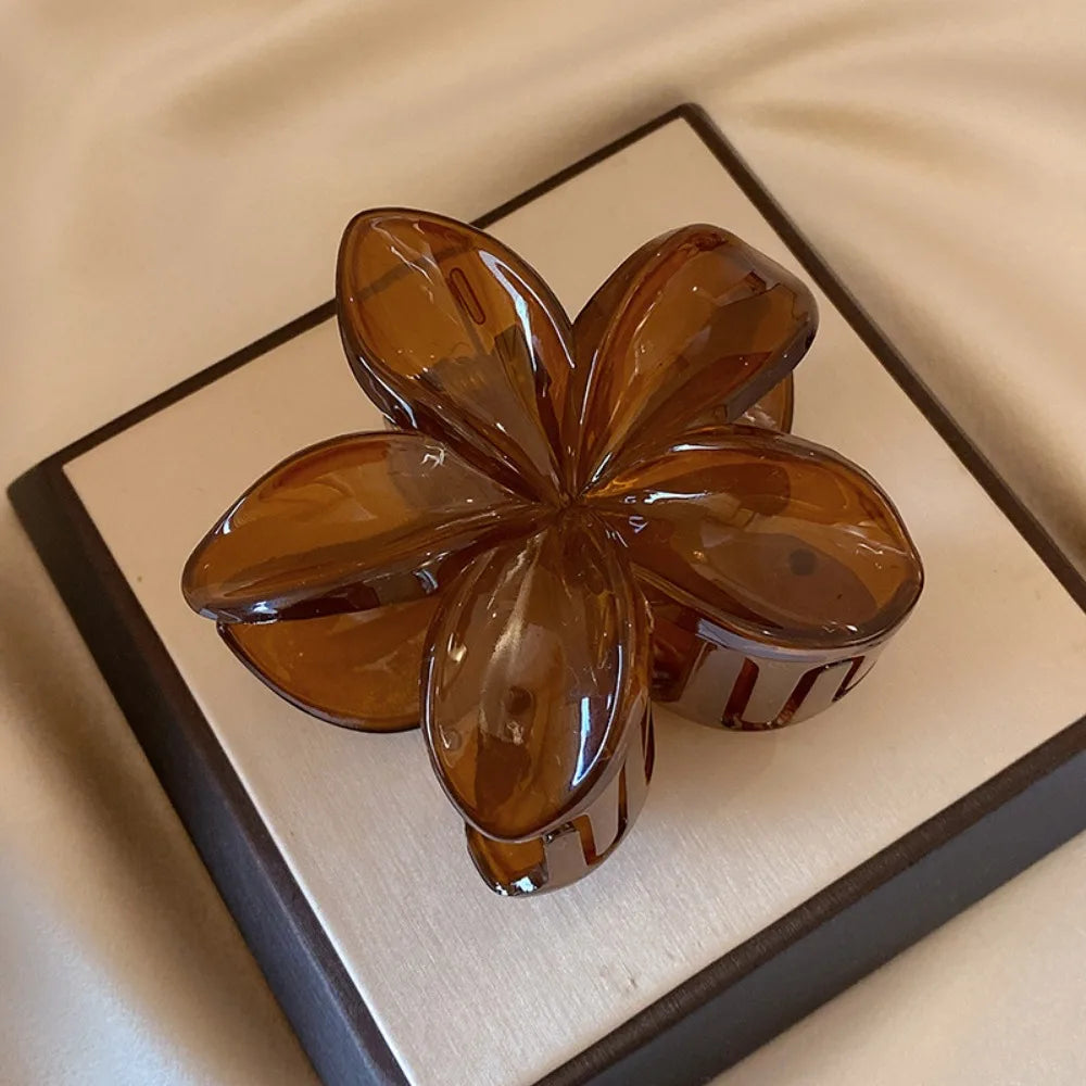 Black 8cm flower-shaped mermaid hair clip with glossy finish on beige display box – lightweight plastic fashion accessory for women.

