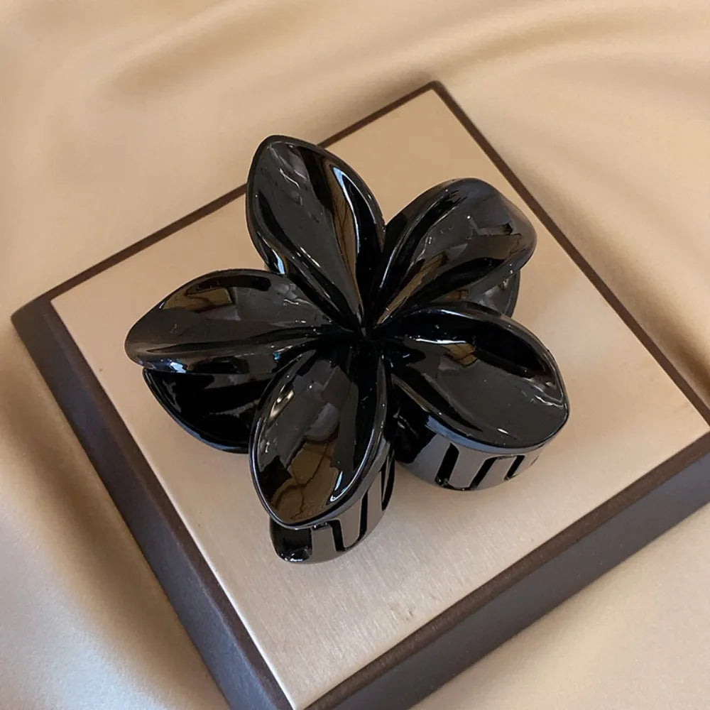 Black 8cm flower-shaped mermaid hair clip with glossy finish on beige display box – lightweight plastic fashion accessory for women.

